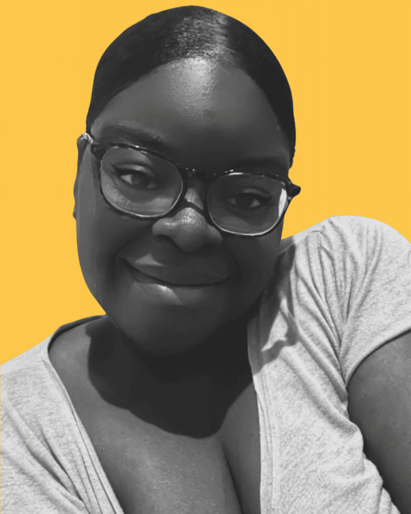 Picture of Brenda Kola. Brenda is a black woman with black hair. She is facing the camera with a smile, her head slightly tilted to her shoulder. She is wearing glasses a t-shirt.