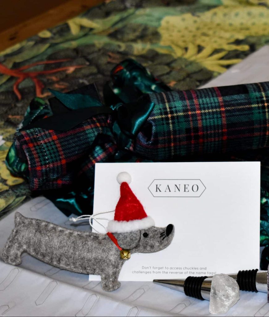 Picture of Kaneo Crackers in dark green with a Kaneo card in front of them and a felt dog with a santa hat on tree decoration.