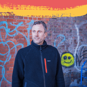 Picture of our CEO, Dirk Bischof in front of a wall with a smiley face sprayed on it.