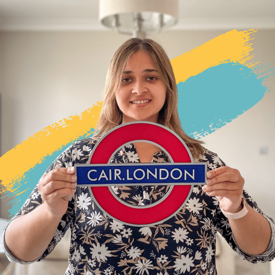 Picture of Tanya Beri, a woman with medium length blonde hair holding a london underground sign with the name of her innovative busines, CAIR London, on it.